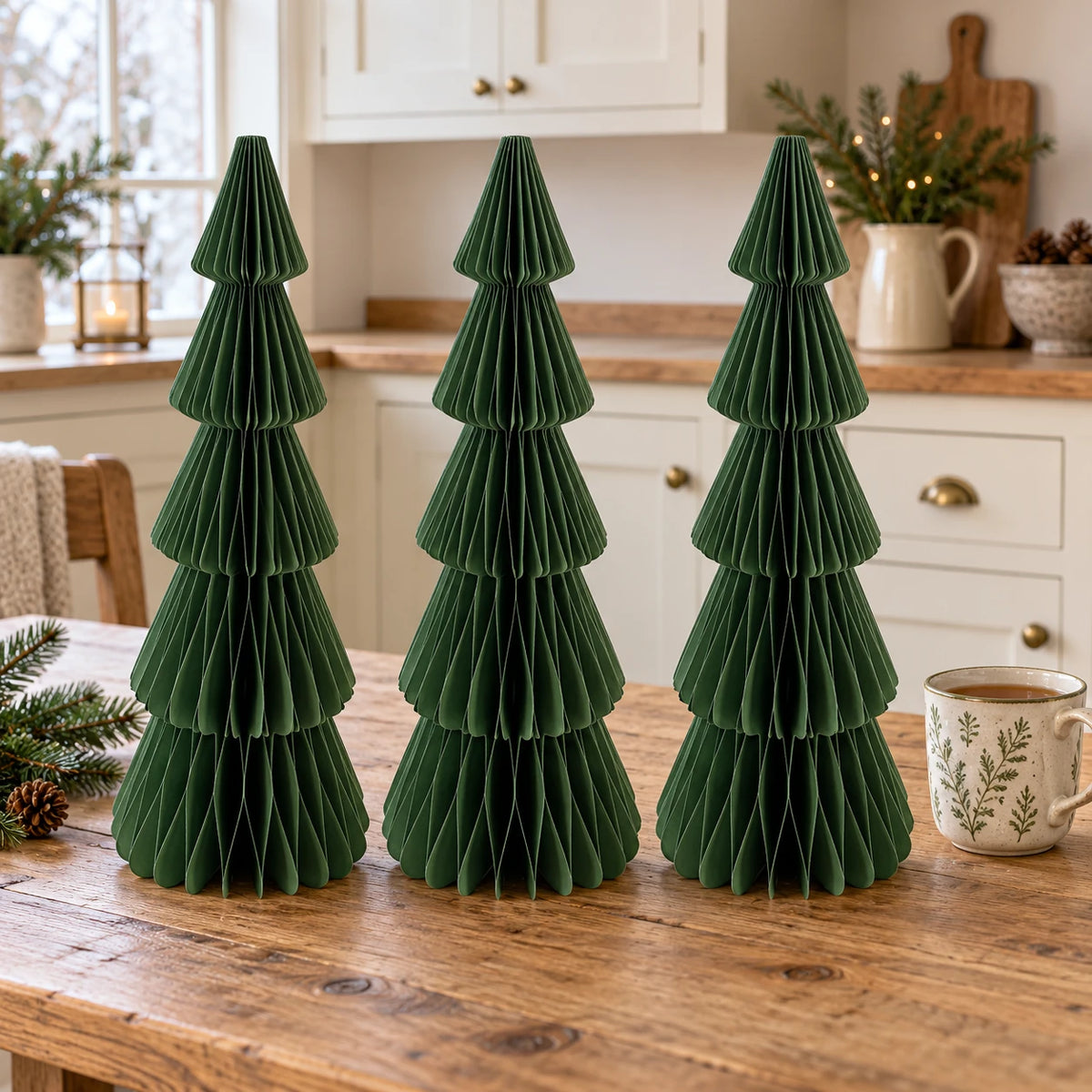 Three matching 30 cm green paper Christmas trees on a kitchen table beside a mug of tea.