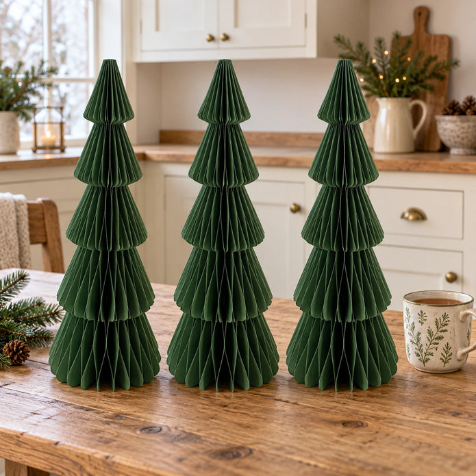 Three matching 30 cm green paper Christmas trees on a kitchen table beside a mug of tea.
