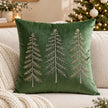 Green velvet cushion cover with three embroidered Christmas trees on a cream sofa beside a decorated Christmas tree.