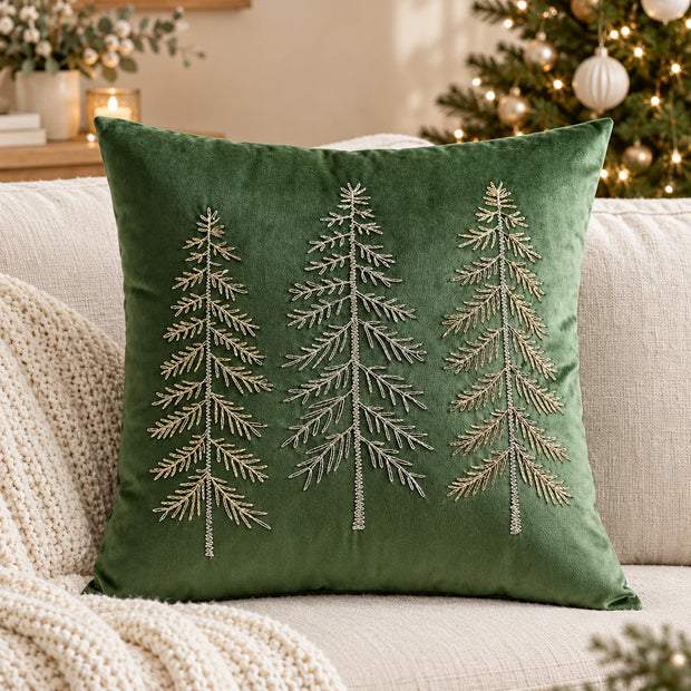 Green velvet cushion cover with three embroidered Christmas trees on a cream sofa beside a decorated Christmas tree.