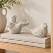 Pair of grey stone bird ornaments styled on oatmeal linen-covered books on an oak shelf.
