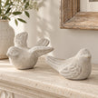 Grey stone birds, one with raised wings and one sitting, displayed together on a cream stone mantel.