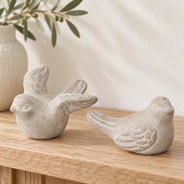 Two grey stone bird ornaments with distressed feather detailing styled on a pale oak console.