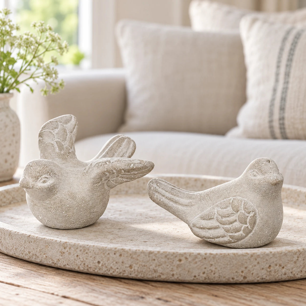 Grey stone bird ornament pair on a pale oval tray, with a cream sofa in the background.