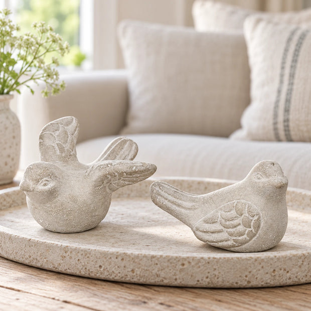 Grey stone bird ornament pair on a pale oval tray, with a cream sofa in the background.