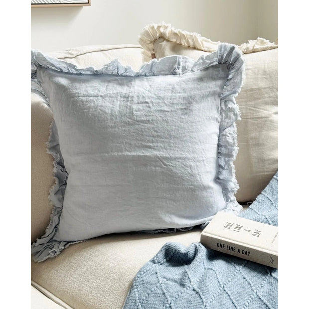 Hallie Ocean Blue Luxury Square Cotton Blend Cushion Cover, pale blue ruffled cushion on a light sofa beside a book