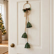 Forest green bells on a hoop hanging from a pale cottage door for Christmas.