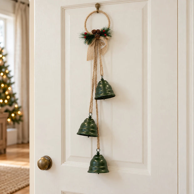 Forest green bells on a hoop hanging from a pale cottage door for Christmas.