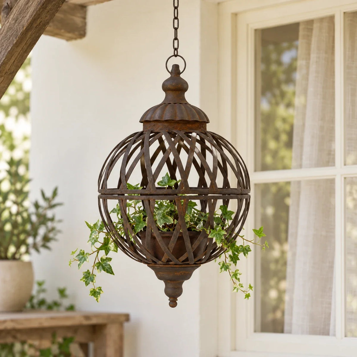 Small rusty lattice ball planter with trailing ivy beside a cream country-home window.