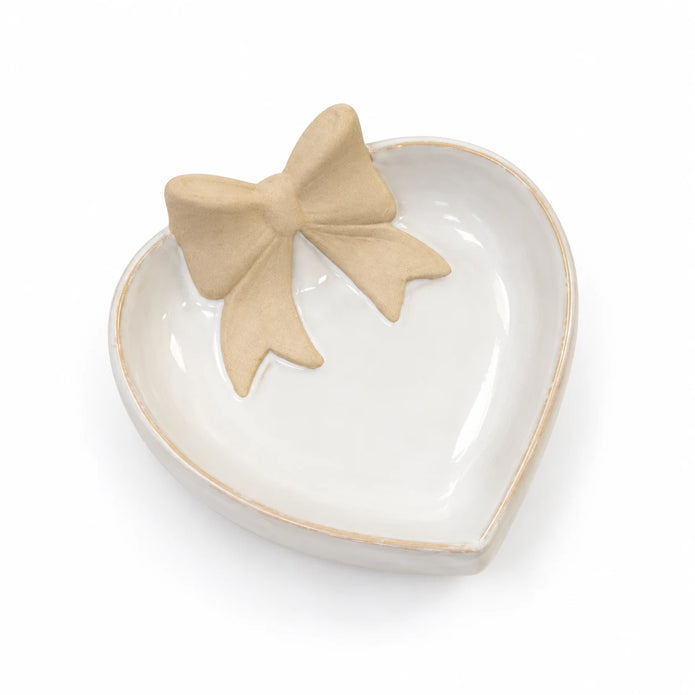 White heart-shaped ceramic dish with beige bow lying flat on a white studio background