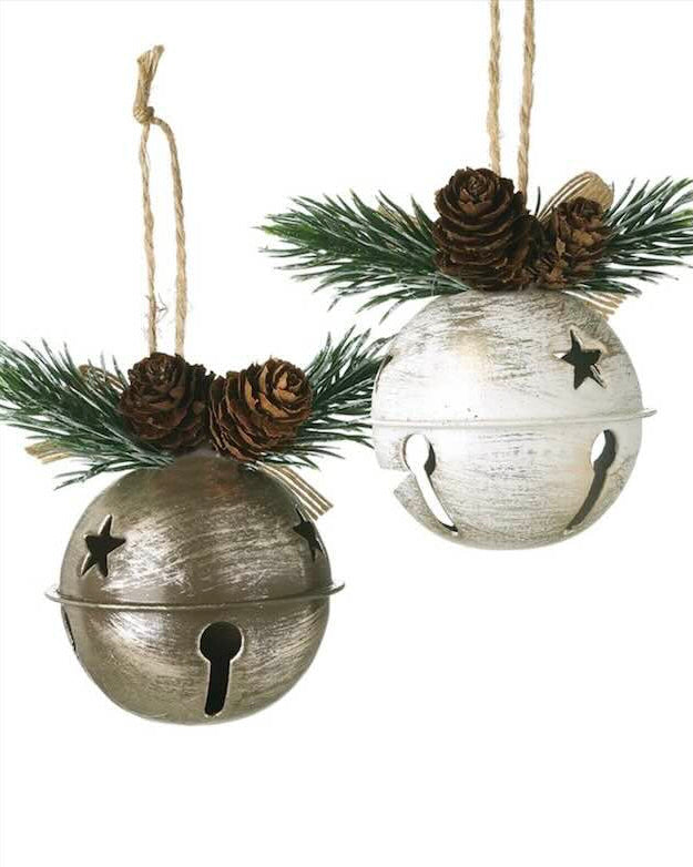 Two rustic bell ornaments with pine cones and greenery on a white background