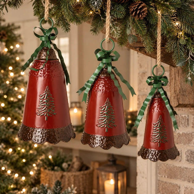 Set of three large red metal Christmas bells with green bows and pine tree detailing hanging from a festive mantel garland