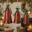 Set of three decorative red Christmas bells with green ribbon bows hung over a rustic fireplace