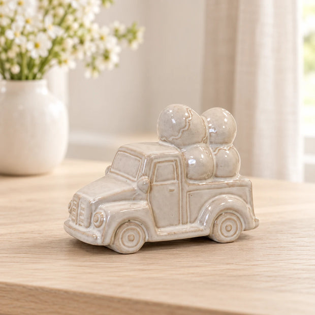 Ivory and stone-toned glazed ceramic car carrying decorative eggs, styled hero view, 13cm wide.
