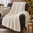 Ivory white faux fur blanket styled on a charcoal armchair beside a Christmas tree