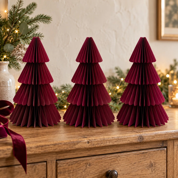 Three matching 30cm burgundy paper Christmas trees on an oak sideboard with festive greenery.