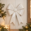 Large white ceramic double bow on cream panelled wall with subtle winter greenery and warm lighting
