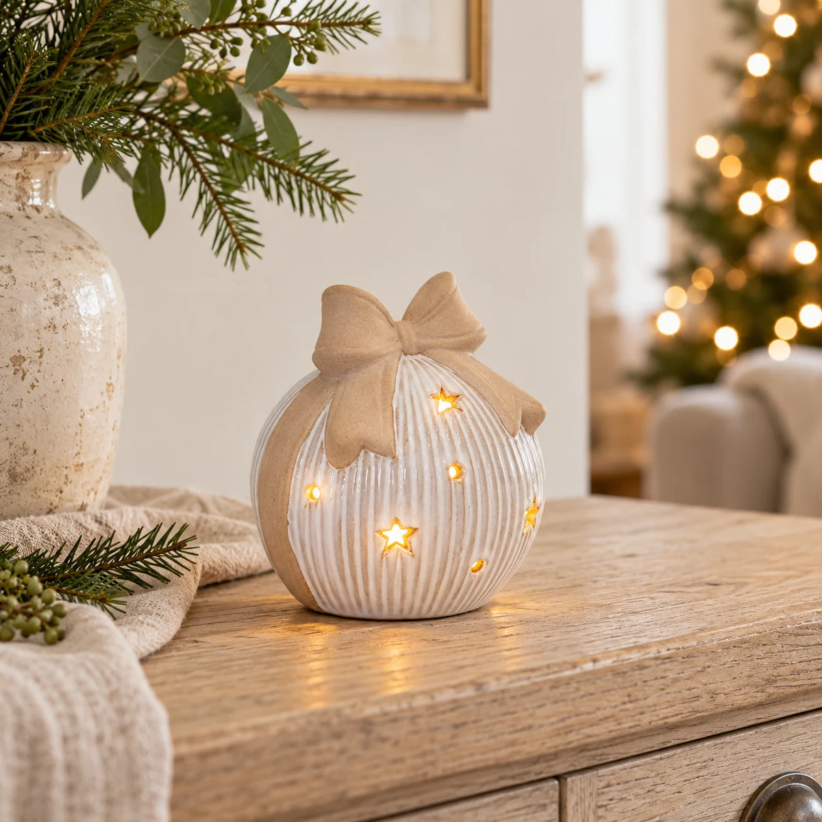 Large white ceramic LED bauble with beige bow glowing on an oak console