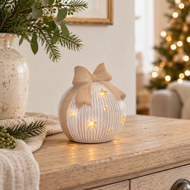 Large white ceramic LED bauble with beige bow glowing on an oak console