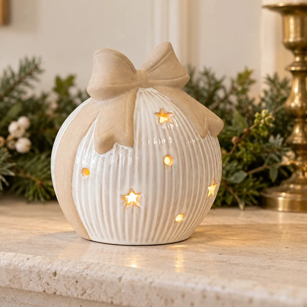 White ribbed ceramic light-up bauble styled with Christmas greenery on a pale mantel