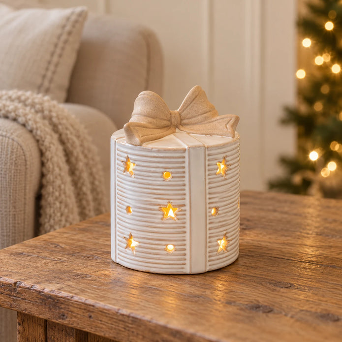 Cream ceramic LED present with a bow topper glowing on an oak side table beside a linen chair