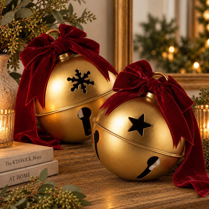 Large gold Christmas bells with burgundy velvet bows resting tilted on a wooden sideboard, star and snowflake designs shown, sold individually