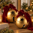 Large gold Christmas bells with burgundy velvet bows resting tilted on a wooden sideboard, star and snowflake designs shown, sold individually