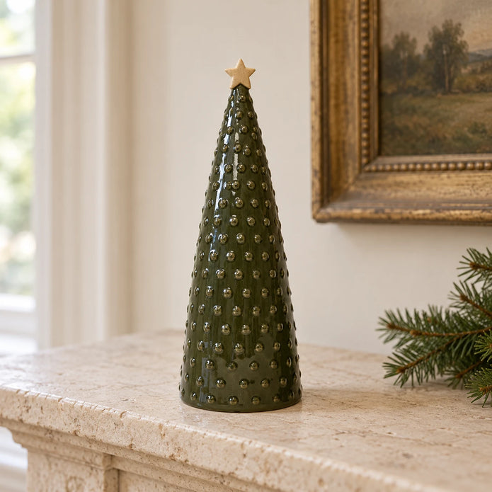 Large green pimpled ceramic Christmas tree displayed on a pale stone mantel beside fir greenery.