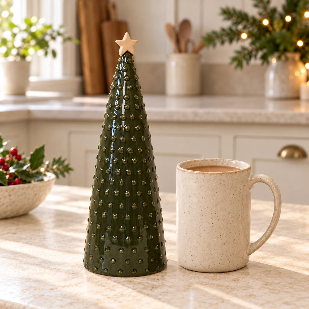 Large green pimpled ceramic Christmas tree beside a cream mug of tea on a country kitchen worktop.