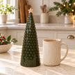 Large green pimpled ceramic Christmas tree beside a cream mug of tea on a country kitchen worktop.