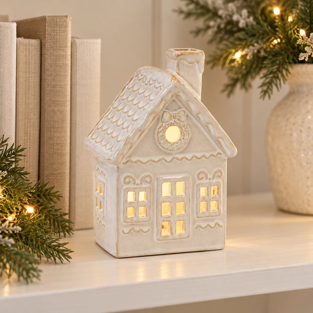 Cream ceramic Christmas house styled beside books on a shelf