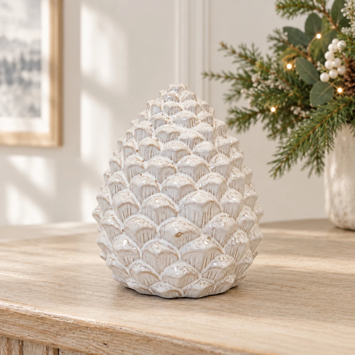 Large ivory glazed ceramic pinecone on an oak console with subtle Christmas greenery