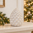Large ceramic pinecone decoration on a limestone mantel in a neutral Christmas room