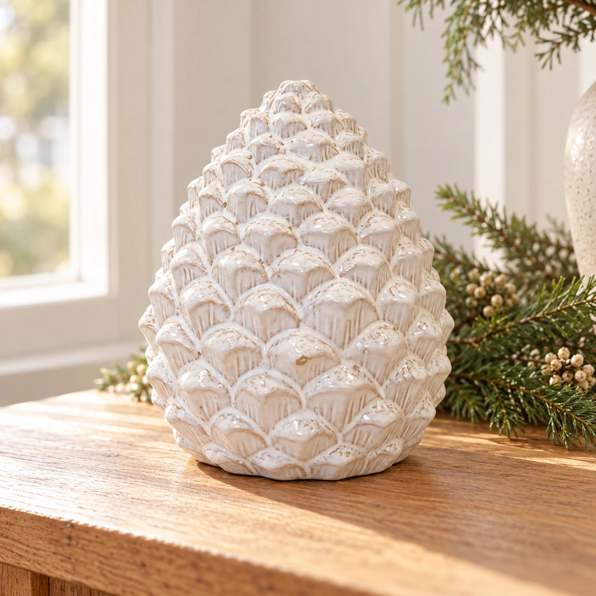 Large ivory ceramic pinecone beside a bright window with evergreen styling