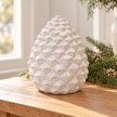 Large ivory ceramic pinecone beside a bright window with evergreen styling