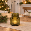 Large olive green candle holder with glowing votive on a neutral Christmas dining table