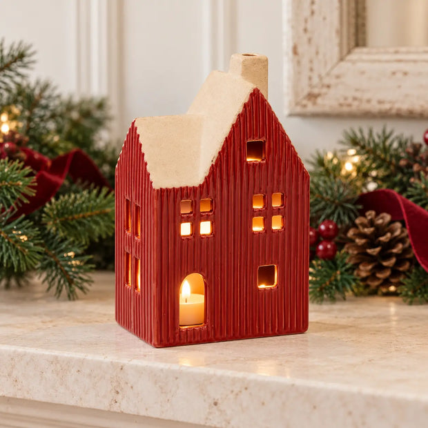 Large red ceramic house tealight holder glowing on a festive cream fireplace mantel