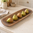 Large rustic wooden dough bowl holding green and russet pears on a cream kitchen worktop.