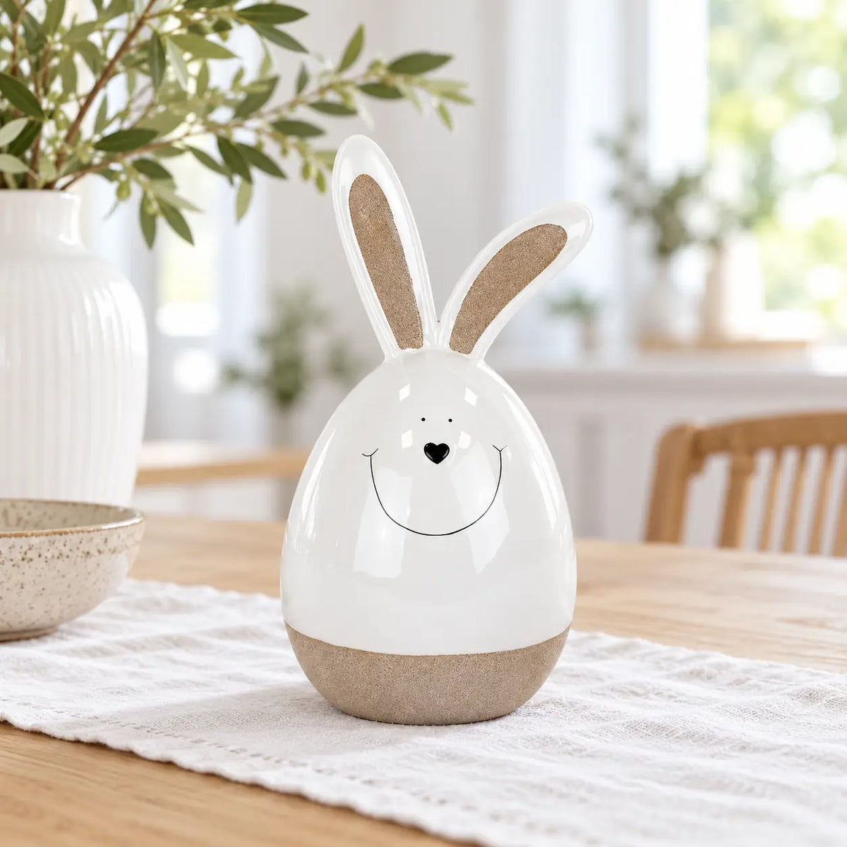 Large white ceramic rabbit with beige ears and base on a linen-covered oak dining table.