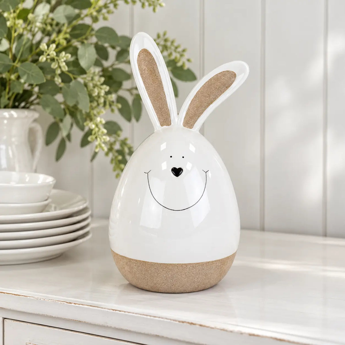 Large white ceramic rabbit beside white crockery on a bright kitchen dresser.