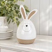Large white ceramic rabbit beside white crockery on a bright kitchen dresser.