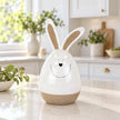Large white ceramic rabbit on a pale kitchen island with soft green foliage in the background.