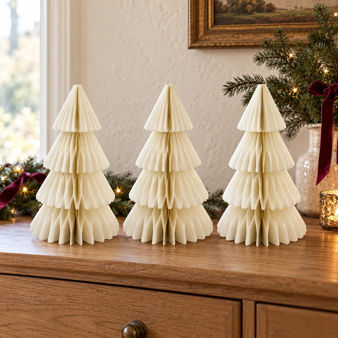 Three matching 30cm winter white paper Christmas trees on an oak sideboard with festive greenery.