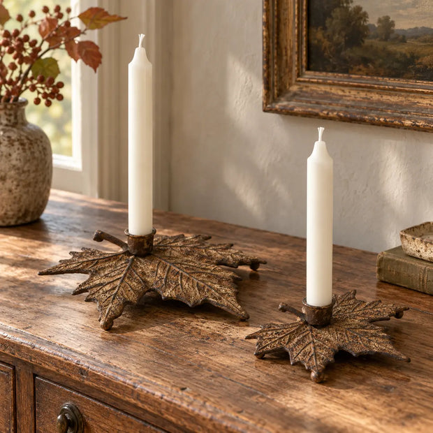 Set of two rust metal maple leaf candle holders styled with unlit ivory taper candles on an antique oak console