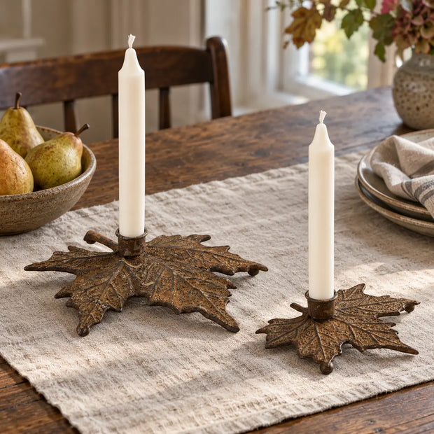 Large and small rust metal leaf candle holders with unlit ivory candles on a natural linen dining table