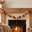 Pinecone and red berry LED garland glowing in a single swag across an oak Christmas mantel.