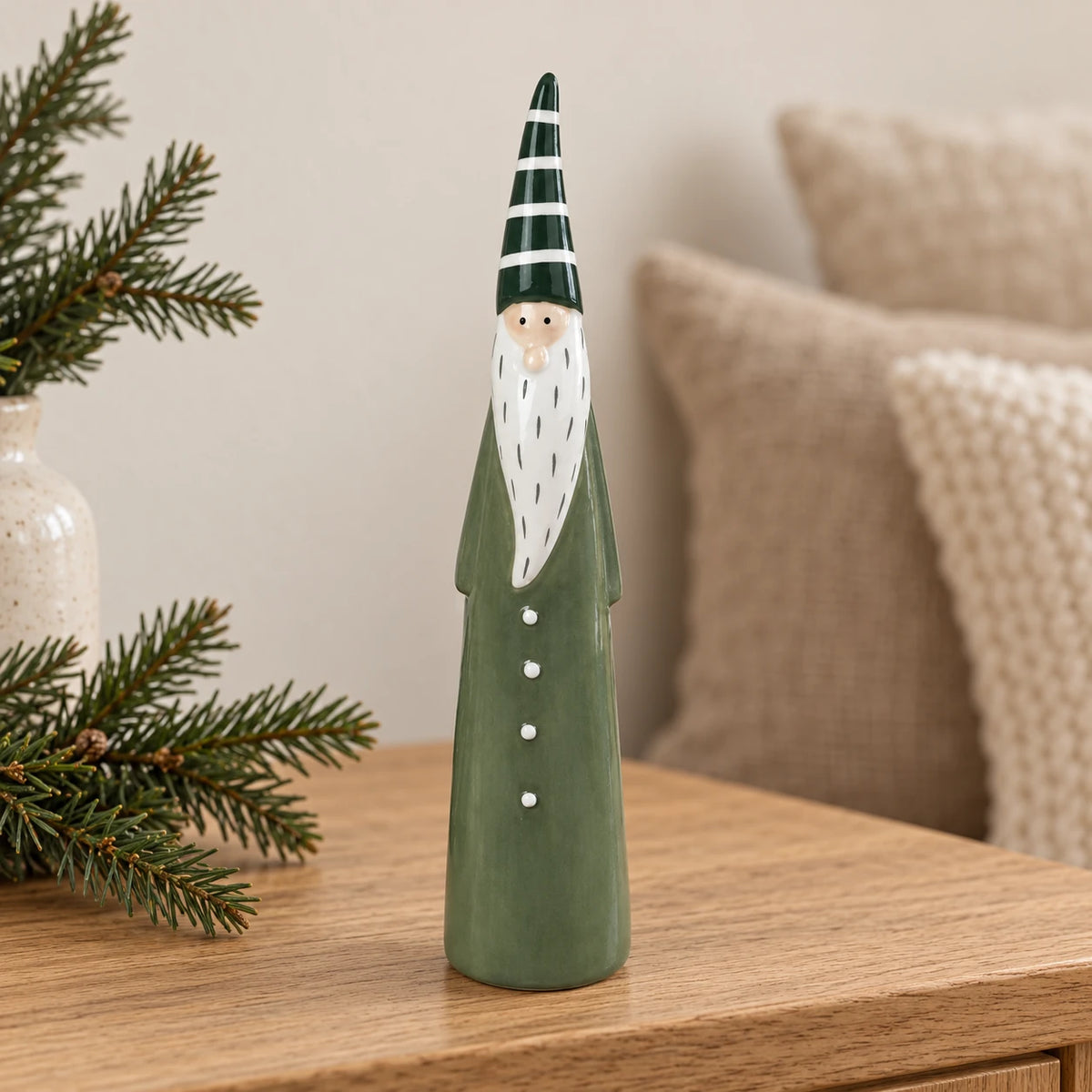 Light green ceramic Christmas gonk with striped hat on an oak console beside winter greenery.