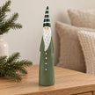 Light green ceramic Christmas gonk with striped hat on an oak console beside winter greenery.