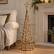 Light up LED rattan Christmas tree with woven star beside a neutral armchair and stone fireplace.