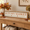 Long Autumn Market Pumpkin Sign on an oak console with autumn foliage.